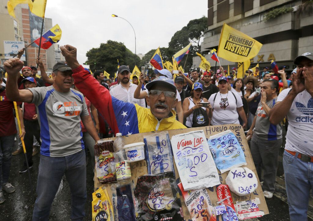 Un opositor sostiene un cartón con bolsas de productos básicos y sus precios durante una protesta contra el presidente venezolano Nicolás Maduero en Caracas, el miércoles 23 de enero de 2019. (AP Foto/Fernando Llano)