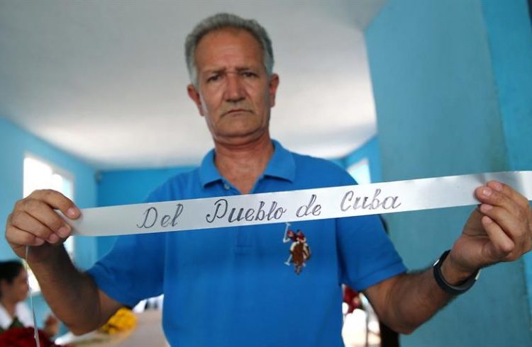 Professor Carlos Parra carefully writes the dedicatory signs on the floral wreaths that accompany the urns of those who died in the plane crash that last Friday plunged into mourning the Cuban province of Holguín, which lost 67 of its sons and daughters in the disaster. Photo: Alejandro Ernesto / EFE.