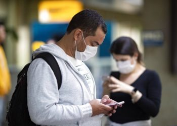 Passengers wearing masks as a precaution against the spread of the new coronavirus use their phones at the International Airport in Sao Paulo, Brazil, on Thursday, February 27, 2020. Photo: Andre Penner / AP.