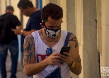 A Cuban checks his cell phone in Havana wearing a facemask as a protection measure against the COVID-19 pandemic. Photo: Otmaro Rodríguez.