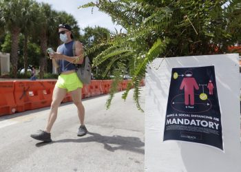 A person wearing a mask walks along Miami Beach, Florida, on Saturday, July 4, 2020. (AP Photo/Wilfredo Lee)