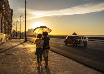 A couple wearing masks hold an umbrella as they walk along the boardwalk at sunset in Havana, Cuba, Monday, Aug. 31, 2020. Photo: Ramón Espinosa/AP