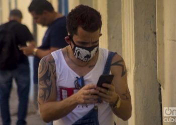 A Cuban man checks his cell phone, wearing a mask in Havana as a protection measure against the COVID-19 pandemic. Photo: Otmaro Rodríguez.