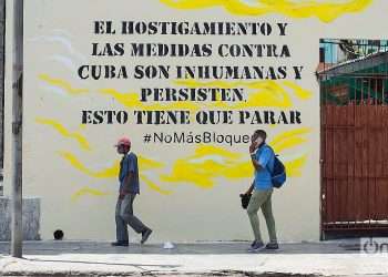 Two men walk past a poster against the U.S. embargo on Cuba, in Havana. Photo: Otmaro Rodríguez.