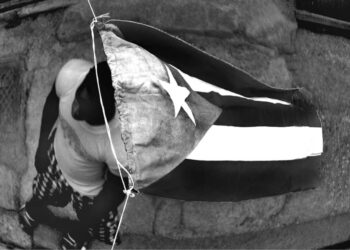 A man walks under the Cuban flag. A holiday in a Havana neighborhood. N/t, Havana, 2009. From the series “Cuba por dentro” (Cuba inside).