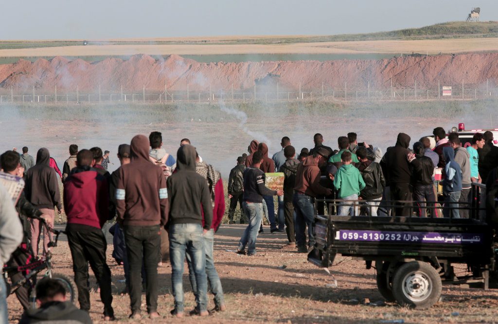 Manifestantes palestinos observan la caída de cargas de gas lacrimógeno disparadas por soldados israelíes durante enfrentamientos en la zona fronteriza de la Franja de Gaza e Israel al este de Beit Lahiya, Gaza, el sábado 31 de marzo de 2018. Foto: Adel Hana / AP.