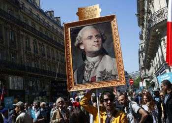 Un manifestante carga un cuadro en el que el presidente de Francia Emmanuel Macron aparece ataviado como el rey Luis 16. El primer año de gobierno de Macron estuvo marcado por una intensa proyección como líder de estatura mundial y protestas en casa por sus reformas económicas y sociales. Algunos de sus detractores le ven aires de autócrata. Foto: Francois Mori/AP.