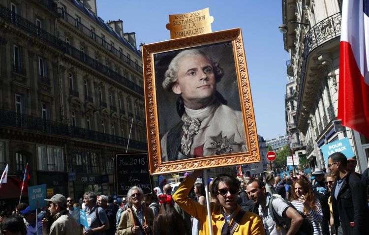 Un manifestante carga un cuadro en el que el presidente de Francia Emmanuel Macron aparece ataviado como el rey Luis 16. El primer año de gobierno de Macron estuvo marcado por una intensa proyección como líder de estatura mundial y protestas en casa por sus reformas económicas y sociales. Algunos de sus detractores le ven aires de autócrata. Foto: Francois Mori/AP.