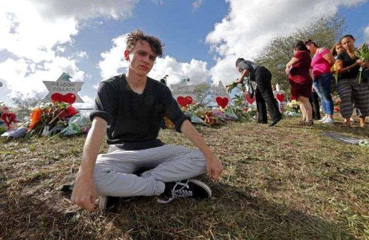 Chris Grady, estudiante de la escuela secundaria Marjory Stoneman Douglas, posa en un memorial en el exterior del centro donde el 14 de febrero de 2018 un pistolero provocó una balacera que causó 17 muertos, en Parkland, Florida. Foto: Gerald Herbert / AP.