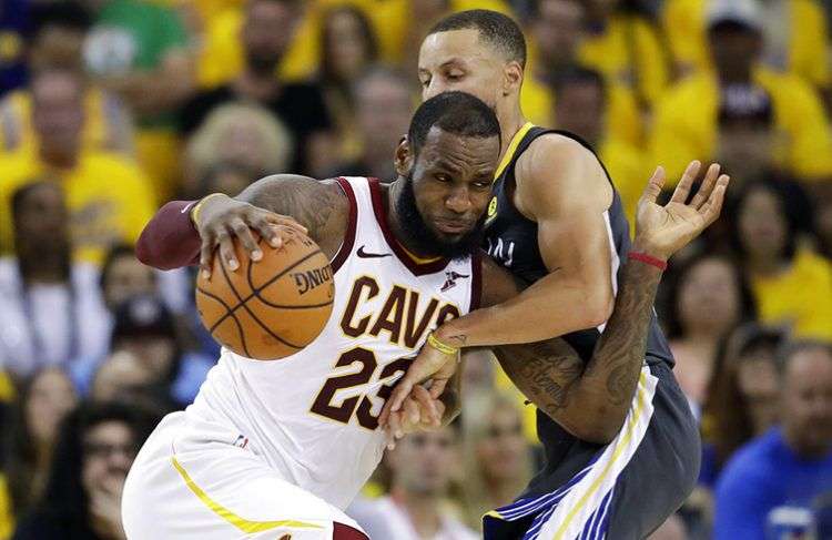 LeBron James (izq), con el uniforme de los Cavaliers de Cleveland, conduce el balón ante la marca de Stephen Curry, de los Warriors de Golden State, durante la final de la NBA de 2018, en Oakland, California. Foto: Marcio Jose Sanchez /AP / Archivo.