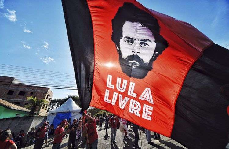 Un partidario del expresidente Luiz Inácio Lula da Silva ondea una bandera con la imagen del exmandatario frente a los cuarteles de la policía federal donde Lula cumple una sentencia de 12 años de prisión, el domingo 8 de julio de 2018. Foto: Denis Ferreira Netto / AP.