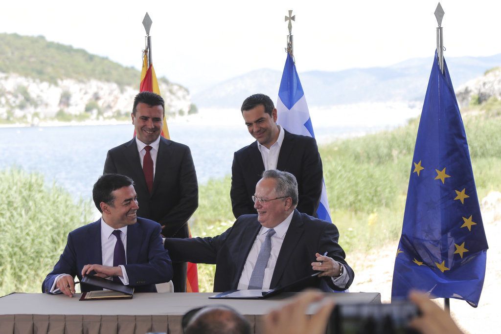 El primer ministro de Grecia, Alexis Tsipras (atrás, derecha), y su homólogo de Macedonia, Zoran Zaev (atrás, izquierda), observan mientras el ministro griego de Exteriores, Nikos Kotzias (derecho), y su contraparte macedonia, Nikola Dimitrov, firman un acuerdo para el nuevo nombre de Macedonia en la localidad de Psarades, en Grecia el 17 de junio de 2018. Foto: Yorgos Karahalis / AP.