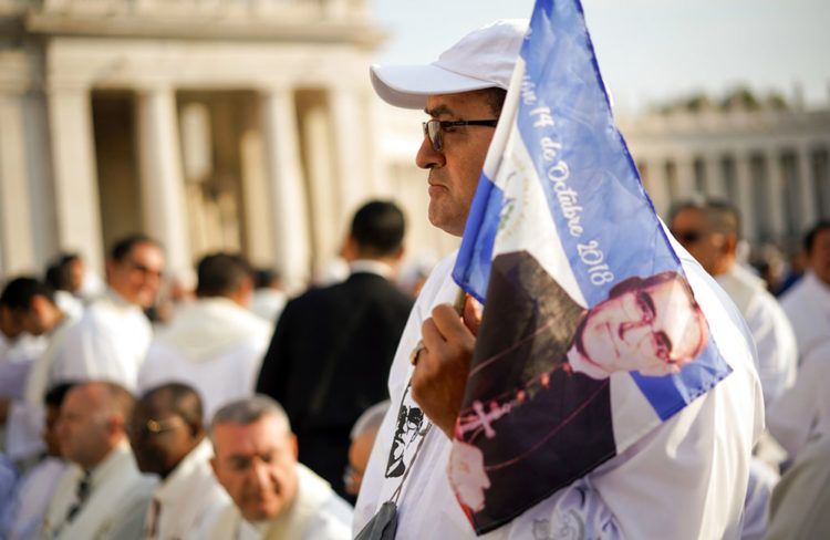 Un hombre sostiene un banderín con la imagen del arzobispo salvadoreño Oscar Romero antes de la ceremonia de canonización en su honor, en la Plaza de San Pedro en el Vaticano, este domingo 14 de octubre del 2018. Foto: Andrew Medichini / AP.