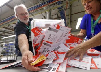 Los trabajadores electorales Mark Bezanson (izquierda) y Julie Olson arrojan sobre una mesa boletas de voto anticipado en la oficina electoral del condado de King, en Renton, Washington, el 5 de noviembre de 2018. Los votantes de Washington votan todos por correo. Foto: Elaine Thompson / AP.