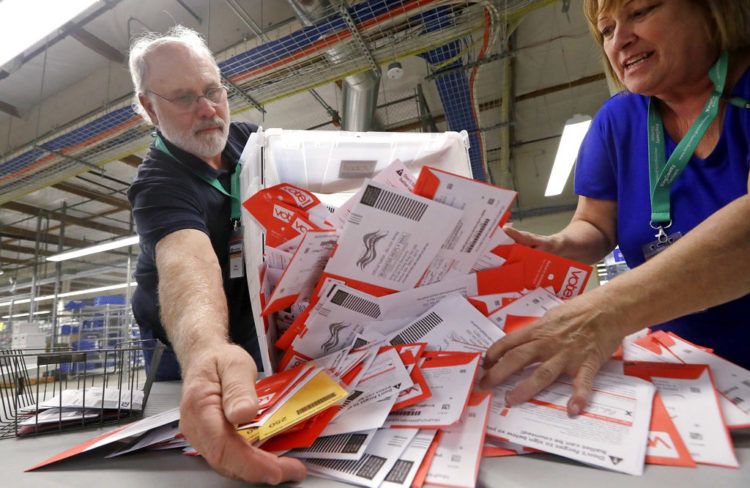 Los trabajadores electorales Mark Bezanson (izquierda) y Julie Olson arrojan sobre una mesa boletas de voto anticipado en la oficina electoral del condado de King, en Renton, Washington, el 5 de noviembre de 2018. Los votantes de Washington votan todos por correo. Foto: Elaine Thompson / AP.