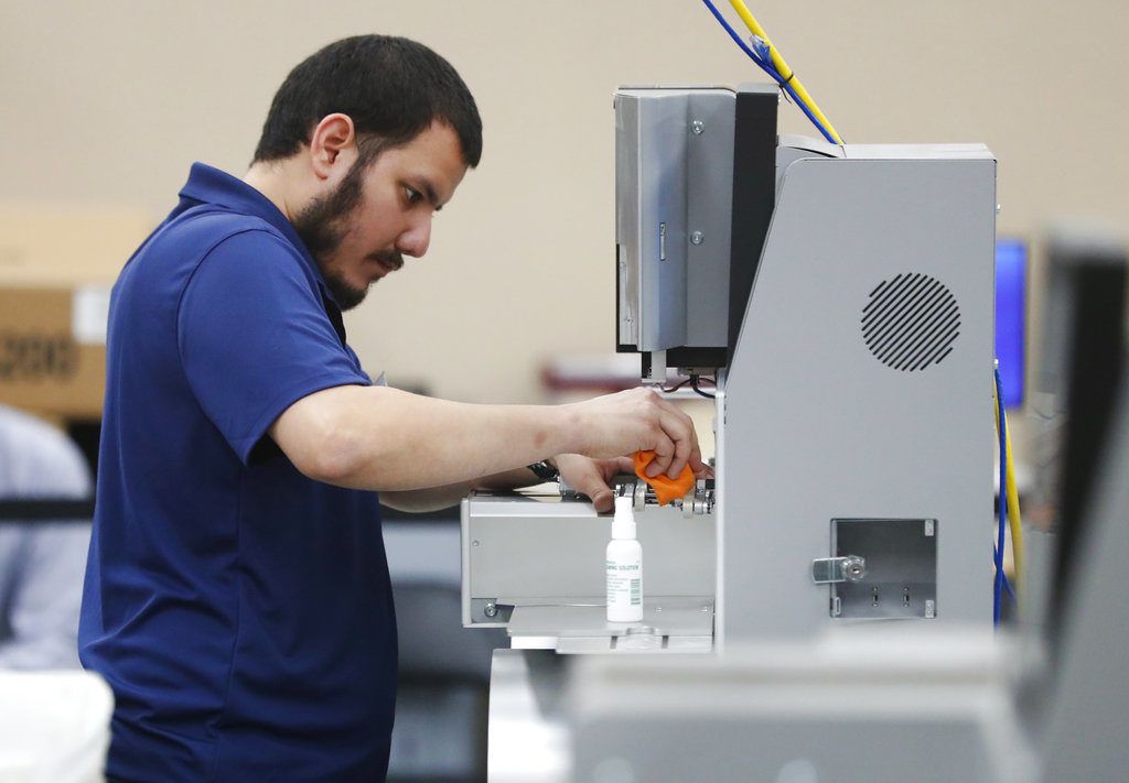 Un trabajador de la oficina de la supervisora de las elecciones del condado de Broward limpia una máquina antes del recuento de votos, el lunes 12 de noviembre de 2018, en Lauderhill, Florida. (AP Foto/Wilfredo Lee)