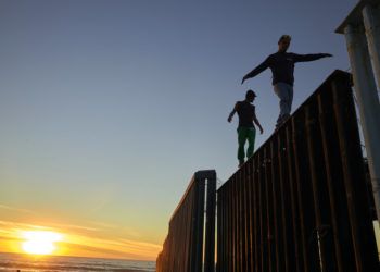 En esta imagen, tomada el 14 de noviembre de 2018, dos migrantes centroamericanos caminan sobre el muro que separa México de Estados Unidos, en Tijuana, México. Integrantes de una caravana de migrantes centroamericanos lograron llegar a la frontera estadounidense tras recorrer los últimos kilómetros de su largo viaje en buses y camiones. (AP Foto/Gregory Bull)