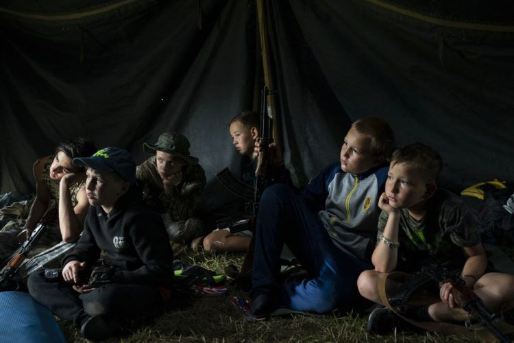 Niños que participan en un campamento de elementos nacionalistas de Ucrania con sus fusiles a su lado escuchan a un instructor el 28 de julio de 2018. En los campamentos les inculcan una ideología nacionalista y les enseñan a combatir a los rusos y sus partidarios. Foto: Felipe Dana / AP.