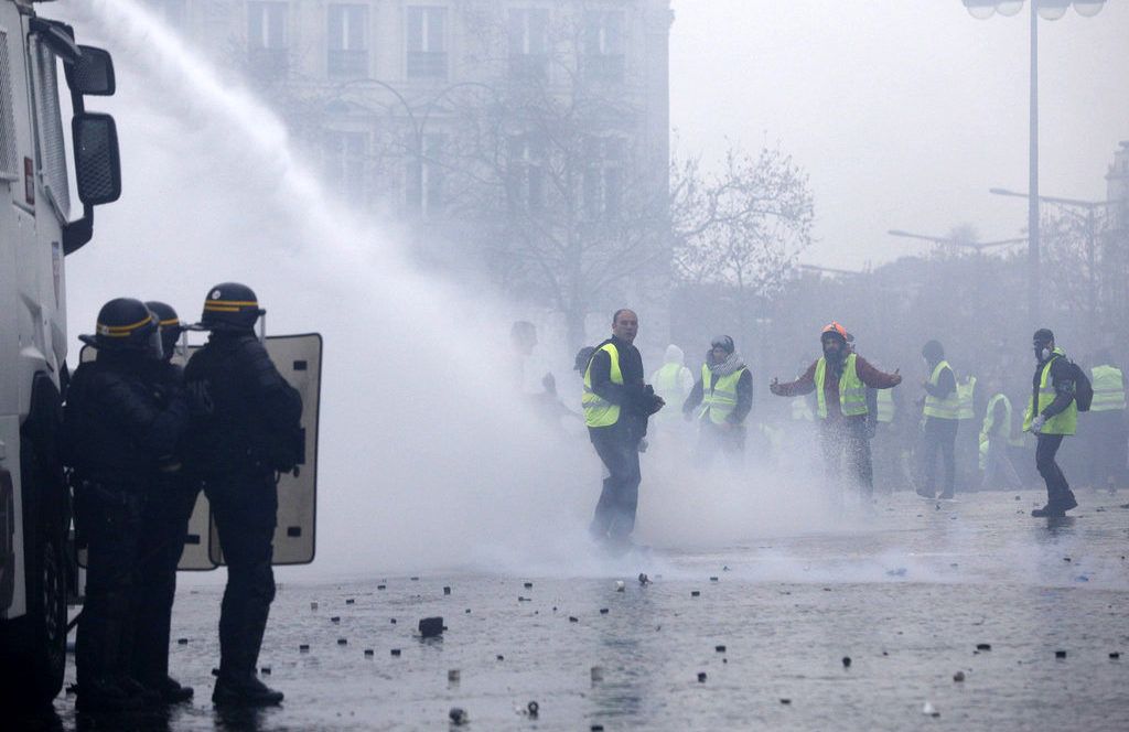 Manifestantes vestidos con chalecos amarillos se enfrentan a los cañones de agua de la policía durante una protesta cerca de la avenida de los Campos Elíseos, en París, el 1 de diciembre de 2018. Foto: Kamil Zihnioglu / AP.