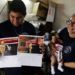 La bombera Fátima Olmedo (derecha) sostiene a su hija de dos meses Samara mientras su esposo, Rodrigo Giménez, muestra las páginas del calendario donde salen desnudos, en Asunción, Paraguay. Foto: Jorge Saenz / AP.