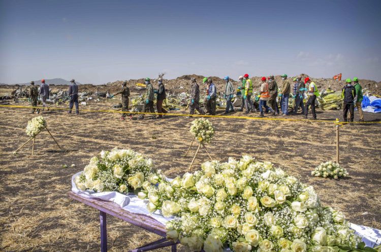 Un grupo de operarios pasa junto a las flores depositadas en el lugar donde se estrelló un Boeing 737 Max 8 de Ethiopian Airlines poco después de despegar con 157 personas a bordo, cerca de Bishoftu, o Debre Zeit, al sur de Adís Abeba, en Etiopía, el 13 de marzo de 2019. Foto: Mulugeta Ayene / AP.