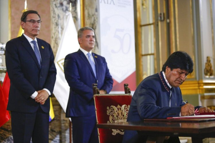 El presidente de Bolivia Evo Morales firma un documento ante la mirada de sus contrapartes Martín Vizcarra, de Perú, e Iván Duque, de Colombia, durante un encuentro de la Comunidad Andina en el 50mo aniversario del organismo, en el palacio de gobierno de Lima, Perú, el domingo 26 de mayo de 2019. Foto: Andre Valle/presidencia de Perú via AP.