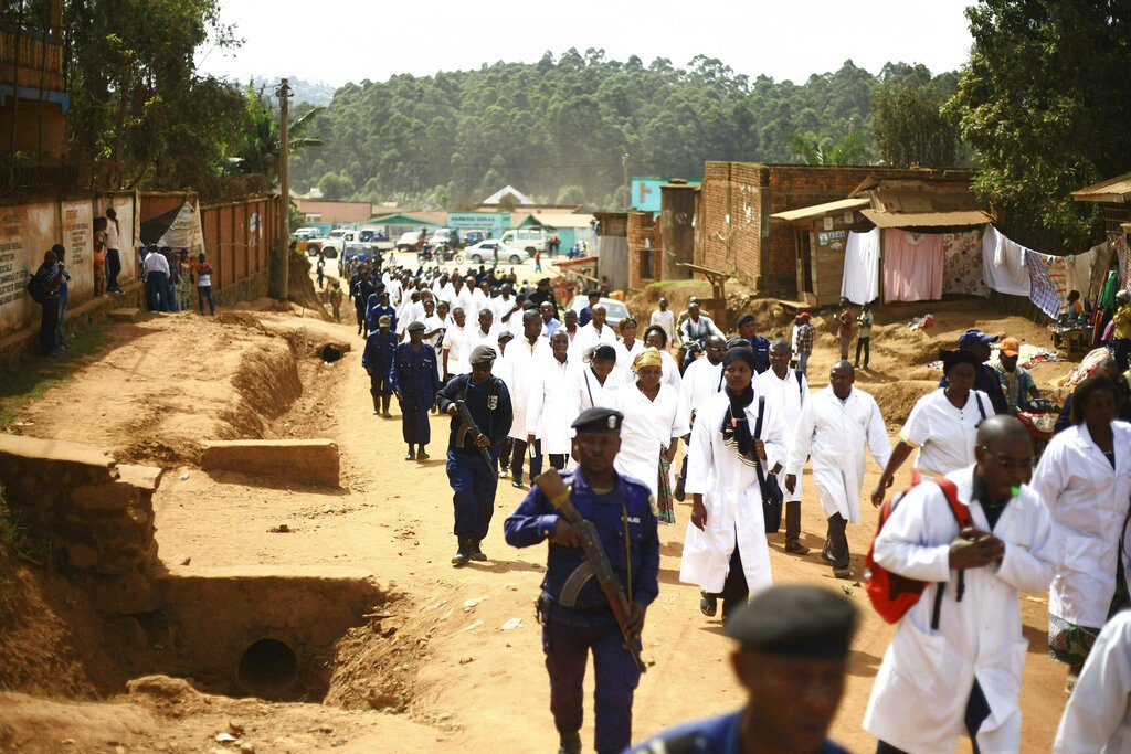 Médicos y trabajadores de salud marchan por la localidad de Butembo, en el este de la República Democrática del Congo, escoltados por fuerzas de seguridad después de que sujetos armados asesinaran a un epidemiólogo camerunés que trabajaba para la Organización Mundial de la Salud en el epicentro de una zona afectada por el ébola. (AP Foto/Al-hadji Kudra Maliro)