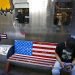 Un hombre navega en su smartphone en una banca decorada con la bandera estadounidense afuera de una tienda que vende marcas de Estados Unidos en un popular centro comercial en Beijing, el lunes 13 de mayo de 2019. (AP Foto/Andy Wong)