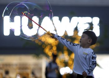 Un niño juega con pompas de jabón cerca del logo del gigante tecnológico chino Huawei, en Beijing, mayo de 2019. Foto: Ng Han Guan / AP.