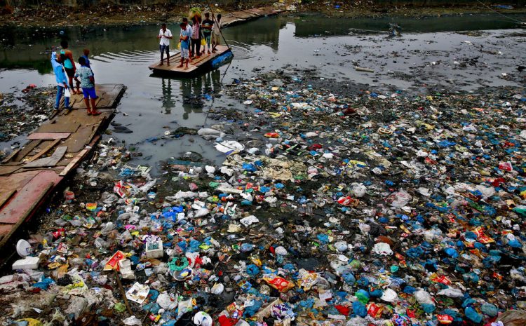 Un hombre conduce una balsa a través de un canal contaminado con bolsas de plástico y otros escombros en Mumbai, India, el 2 de octubre de 2016. Foto: Rafiq Maqbool / AP.