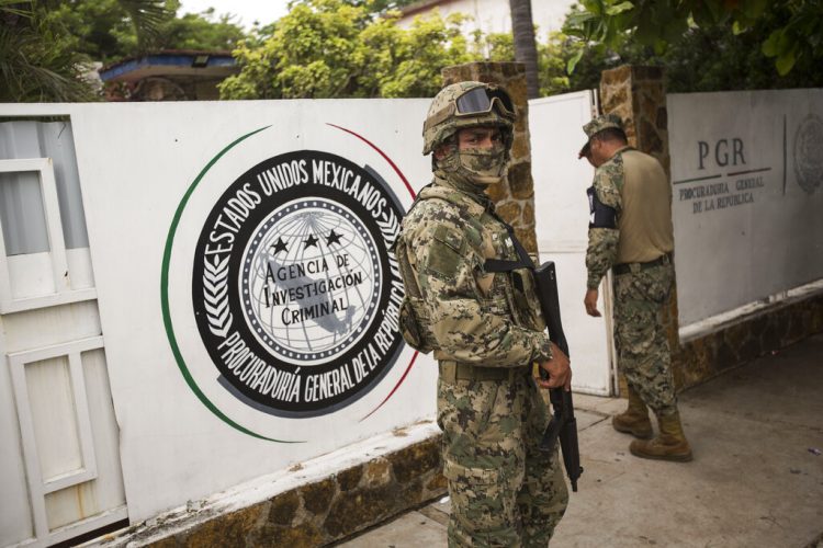 Un infante de Marina, al frente, y un miembro de la Guardia Nacional, atrás, vigilan afuera de una oficina de la Procuraduría General de la República adonde son enviados los migrantes antes de ser transferidos a Tapachula desde Arriaga, México, el domingo 23 de junio de 2019. Foto: Oliver de Ros / AP.