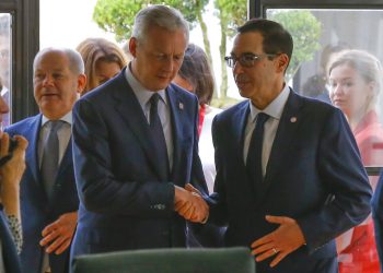 El ministro francés de Finanzas, Bruno Le Maire, a la izquierda, estrecha la mano con el secretario del Tesoro de Estados Unidos, Steve Mnuchin, junto al ministro alemán de Finanzas, Olaf Scholz, al fondo a la izquierda, durante una reunión de los responsables de finanzas del G7 en Chantilly, al norte de París, el jueves 18 de julio de 2019.  Foto: Michel Euler/ AP.