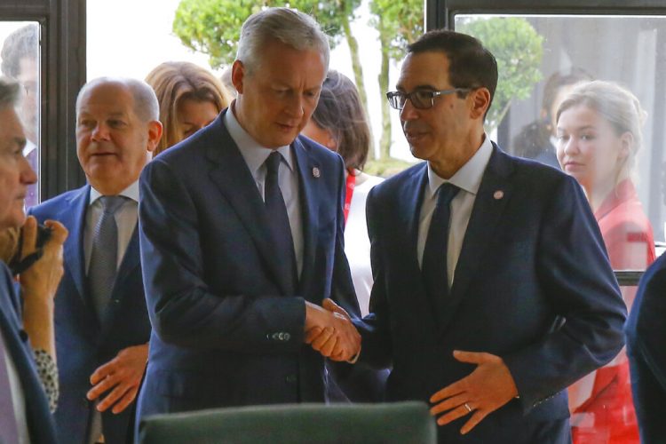 El ministro francés de Finanzas, Bruno Le Maire, a la izquierda, estrecha la mano con el secretario del Tesoro de Estados Unidos, Steve Mnuchin, junto al ministro alemán de Finanzas, Olaf Scholz, al fondo a la izquierda, durante una reunión de los responsables de finanzas del G7 en Chantilly, al norte de París, el jueves 18 de julio de 2019.  Foto: Michel Euler/ AP.