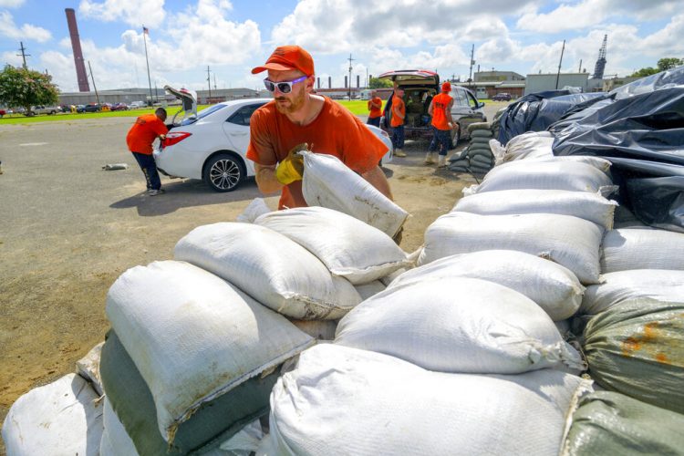 Trabajadores reclusos del departamento de policía de la municipalidad de St. Bernard trasladan costales de arena para los residentes en Chalmette, Luisiana, el jueves 11 de julio de 2019. Foto: Matthew Hinton / AP.