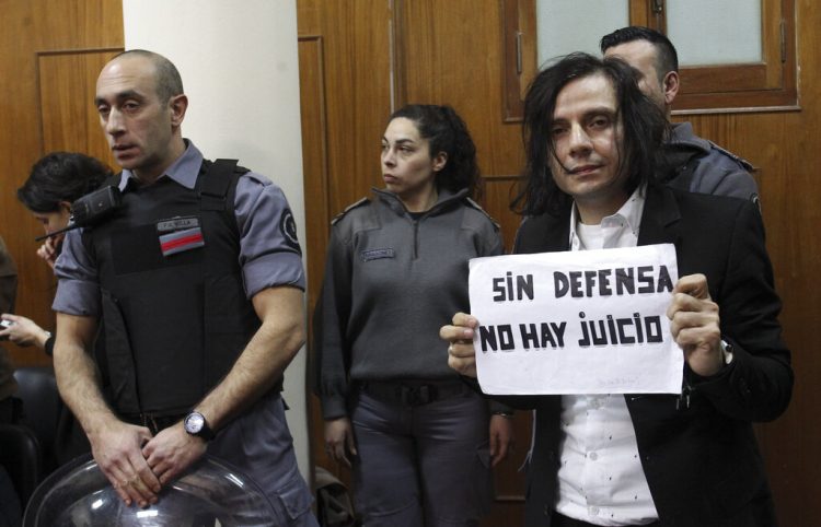 Cristian Aldana, vocalista principal de la banda de rock argentina El Otro Yo, posa durante su juicio por presunto abuso sexual de menores con un cartel que dice "Sin defensa no hay juicio" el viernes 12 de julio del 2019 en Buenos Aires. Foto: Bernardino Avila/ AP.