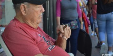 Un cubano fuma un tabaco y dormita frente a su negocio en la Calle Ocho. Foto: Marita Pérez Díaz.