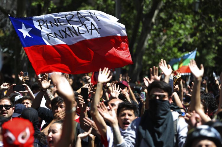 Los manifestantes ondean una bandera chilena pintada con el mensaje "Piñera renuncia" durante una manifestación en Santiago, Chile, el lunes 21 de octubre de 2019. (AP Foto / Miguel Arenas)