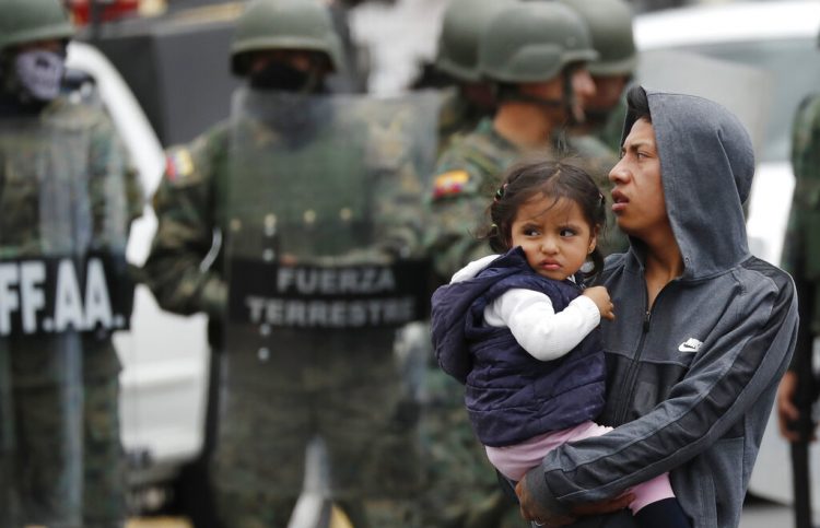 Un hombre que carga a una niña sale de un camino bloqueado durante las protestas contra el presidente Lenín Moreno, después de que soldados llegaran a reabrirlo en Quito, Ecuador, el lunes 7 de octubre de 2019. Foto: Dolores Ochoa / AP.