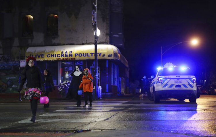 Personas disfrazadas que piden dulces por Halloween caminan en la calle 26 West junto al lugar donde una niña de 7 años fue baleada mientras hacía lo mismo, el jueves 31 de octubre de 2019, en Chicago. (John J. Kim/Chicago Tribune vía AP)