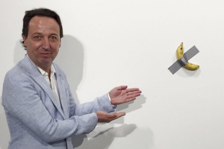 En esta foto del 4 de diciembre del 2019, el dueño de galería Emmanuel Perrotin posa junto a la obra "Comedian" del artista italiano Maurizio Cattlelan durante su exhibición en la feria Art Basel Miami, en Miami Beach, Florida. La obra se vendió por 120.000 dólares. (Siobhan Morrissey vía AP)
