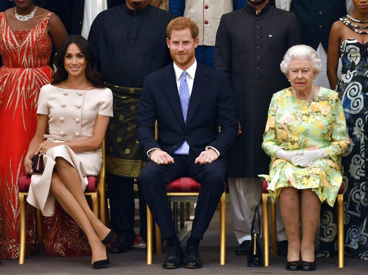 El príncipe Enrique, su esposa Meghan Markle (izq) y su abuela, la reina Isabel II, fotografiados durante una ceremonia en el Palacio de Buckingham el 26 de junio del 2018. En un comunicado enviado el lunes 13 de enero de 2020 la reina Isabel II dijo que accedió a conceder el deseo del príncipe Enrique y Meghan para una vida más independiente en la que residirán parcialmente en Canadá. (John Stillwell/Pool Photo via AP, archivo)