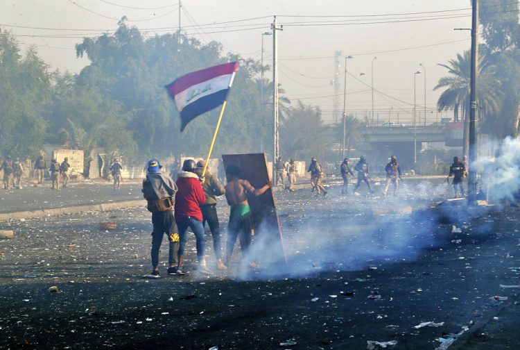 Manifestantes ondeando la bandera nacional mientras las fuerzas de seguridad lanzan gas lacrimógeo a una protesta en el centro de Bagdad, Irak, el lunes 20 de enero de 2020. Foto: AP/Hadi Mizban