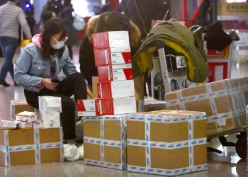 Una viajera sentada junto a cajas de mascarillas para la cara y respiradores en el aeropuerto internacional de Beijing, el 30 de enero de 2020. Foto: Mark Schiefelbein / AP.