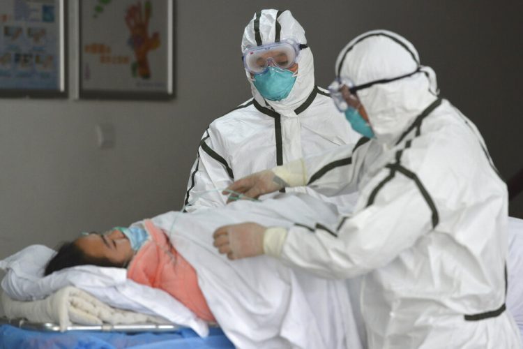 Personal sanitario provisto con trajes protectores traslada a una paciente infectada con coronavirus a un pabellón de aislamiento en el Segundo Hospital del Pueblo en Fuyang, provincia de Anhui, en el centro de China, a inicios de la pandemia. Foto: Chinatopix vía AP.