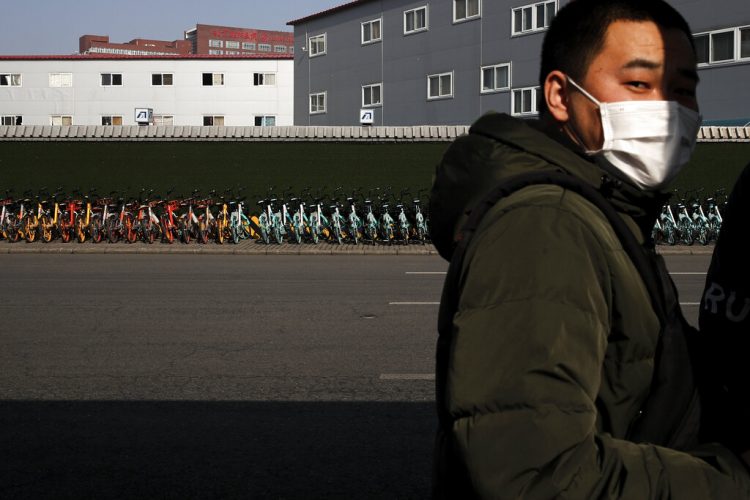 Un hombre con mascarilla junto a una fila de bicicletas de alquiler estacionadas ante una estación de metro en Beijing, el lunes 10 de febrero de 2020. (AP Foto/Andy Wong)