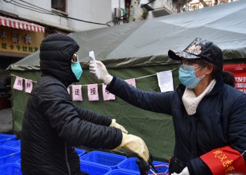 Una mujer revisa la temperatura a un ciclista que porta una mascarilla en la ciudad de Wuhan. Foto: Chinatopix vía AP/Archivo.