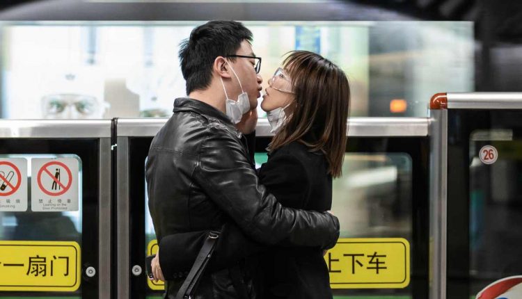 Una pareja se quita las mascarillas de seguridad y se besa mientras espera el transporte público en Shanghái, China. Foto: Liu Xingzhe / EFE: