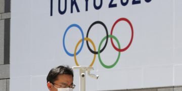 Un hombre con una mascarilla pasa junto a un cartel que anuncia los Juegos Olímpicos de Tokio del 2020, ya pospuestos para el próximo año. Foto: Koji Sasahara / AP / Archivo.