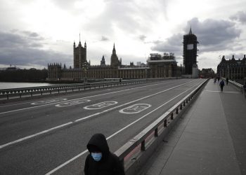 Una persona con una mascarilla en el rostro camina por el puente de Westminster casi vacío con el Parlamento al fondo. Londres, viernes 20 de marzo de 2020. Foto: Matt Dunham/AP.