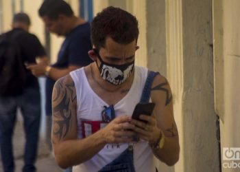 Un cubano revisa su celular usando un nasobuco en La Habana, como medida de protección frente a la pandemia de COVID-19. Foto: Otmaro Rodríguez.